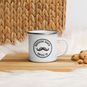 White 12 oz. Mustache Ranch Coffee Co. enamel mug with black logo, displayed on a wooden surface with a woven basket and cookies, styled for a rustic, farmhouse aesthetic.